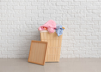 Wooden basket with dirty clothes near white brick wall