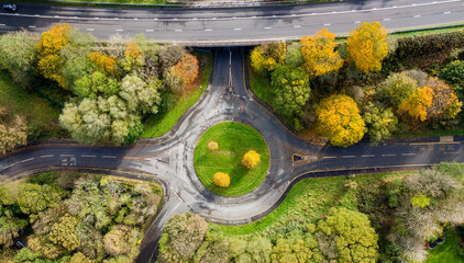 Aerial view of a small traffic roundabout surrounded by colourful trees displaying autumn colours