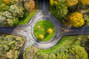 Aerial view of a small traffic roundabout surrounded by colourful trees displaying autumn colours © whitcomberd
