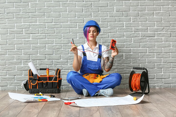 Female electrician with multimeter meditating near brick wall