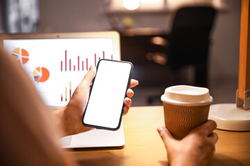 Young woman using mobile phone and holding paper cup of coffee in office