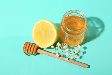 Jar of sweet honey, dipper and lemon on color background