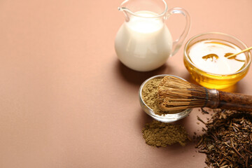 Bowl with hojicha powder, honey, jug of milk and chasen on brown background