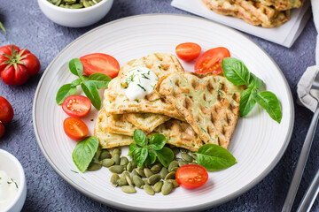 Ready-to-eat delicious zucchini waffles, tomatoes, basil and pumpkin seeds on a plate on the table. Vegetable diet food. Close-up