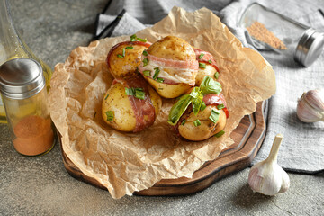 Wooden board of tasty baked potatoes with bacon on grunge background
