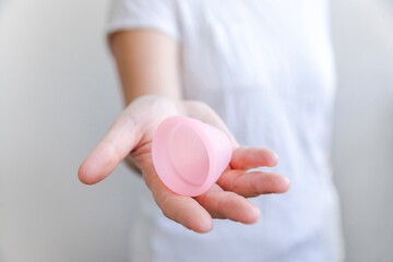 Woman hand holding pink menstrual cup Isolated on white background. Woman modern alternative eco gynecological hygiene in menstruation period. Container for blood in girl hand. - obrazy, fototapety, plakaty