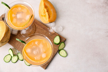 Glasses of cold cocktail, slices of cucumber and melon on light background