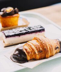 Un croasan, una porcion de cheesecake y un muffin de carrot cake en una pasteleria