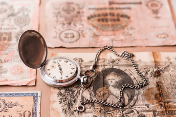 Old worn out of circulation ruble banknotes of tsarist russia and a watch on a chain on a brown background