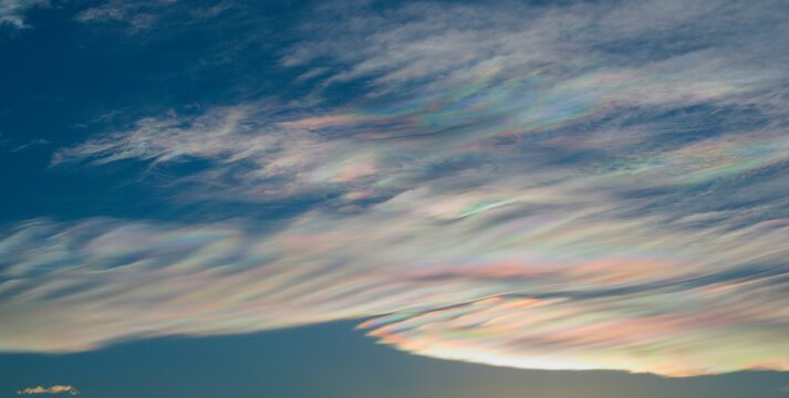Thin wispy clouds creating rainbow patterns of scattered sunlight. Optical phenomenon on cirrostratus clouds.