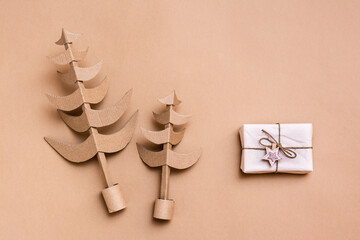 Christmas trees made of cardboard and a gift in craft paper on a beige background. Eco-friendly decorations for the holiday.