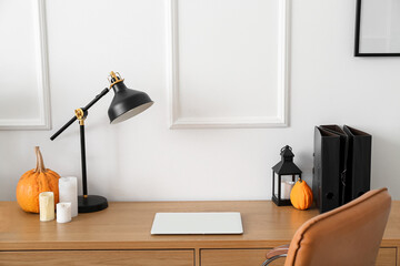Modern workplace with Halloween pumpkins and candles near light wall