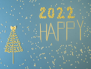 Naklejka premium Christmas tree lined with dry pasta and numbers 2022 and stars from pasta on a blue paper background.