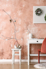 Tree branches with Christmas balls in vases on tables near pink wall