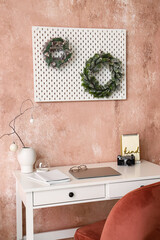 Modern workplace and Christmas wreaths near pink wall