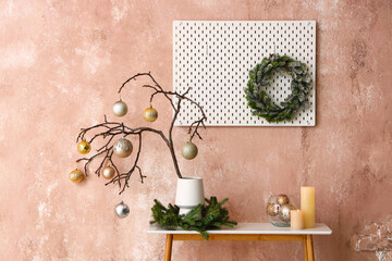 Tree branches with Christmas balls in vase and candles on table near pink wall
