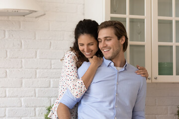 Young millennial 30s beautiful couple in love cuddling standing in modern cozy renovated kitchen. Bank loan, happy homeowners family, relocation and tenancy, romantic date and relationships concept
