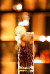 Glass of tasty Cuba Libre cocktail on table against blurred lights