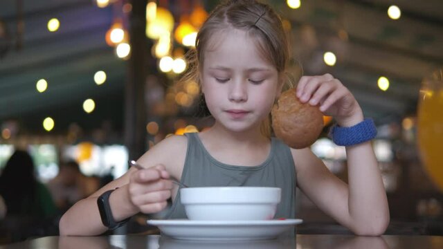 Child girl eating soup and tasty burger in restaurant