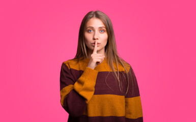 Serios young woman makes the shh gesture while looking at the camera.