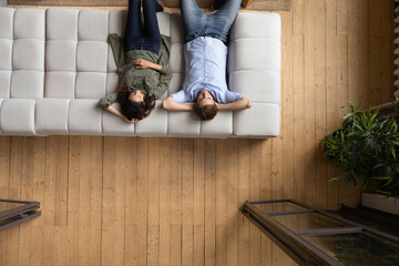 Serene couple put hands behind head relaxing on cozy sofa, above view. Homeowners family enjoy rest...
