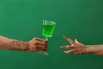 Hands of zombies with glass of cocktail on color background