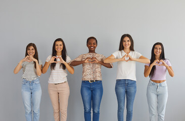 Studio group portrait of happy smiling thankful young diverse multiracial women standing together, doing heart shape hand gesture, sharing positive emotions and sending you love, support and gratitude