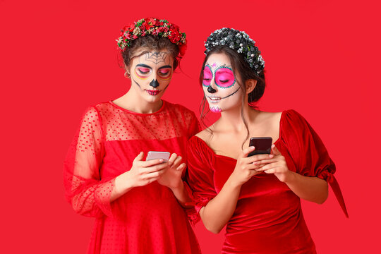 Stylish women with painted skull on faces and mobile phones against color background. Celebration of Mexico's Day of the Dead (El Dia de Muertos)