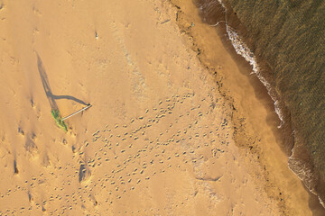 Aerial shot of fallen umbrella and footprints on a beach in Greece