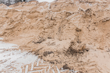 A large pile of sand of natural industrial material is stored outdoors on the territory of the plant