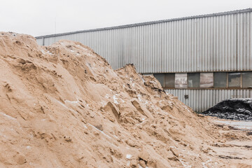 A large pile of sand of natural industrial material is stored outdoors on the territory of the plant