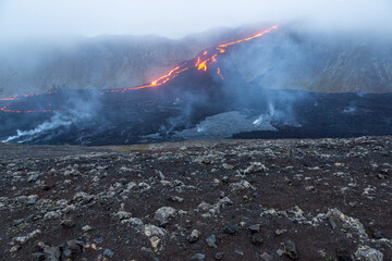 Obraz premium Lava flow from the Fagradsfjall volcano in Iceland. Lava is deep orange color surrounded by dark black lava rock with brown lava rocks in foreground. Steam rising from the ground.