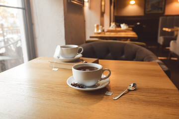 White cup of hot tea with bag and spoon on table in cafe