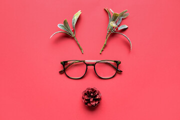 Creative Christmas composition with reindeer face made of glasses, pine cone and flowers on red...