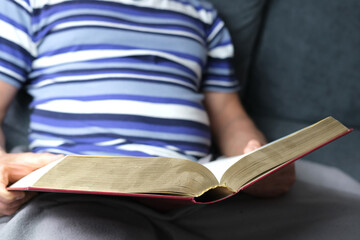 close-up of thick book in dark red cover, family bible, old man, senior reads, concept eternal...