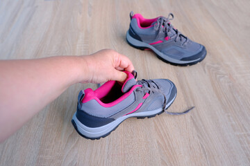 female hands inspecting a pair of gray new womens trekking shoes with pink trim, tied with laces,...