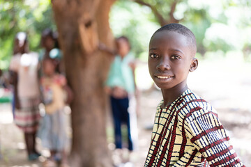 Portrait of a cute black African boy with freshly shaved hair, smiling at the camera, with a group...