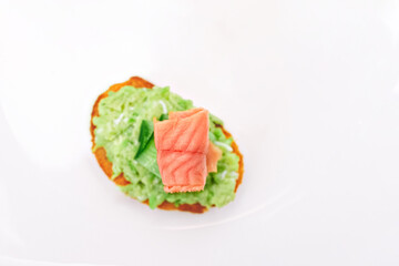 red fish on sandwich with guacamole, cucumber in blur on white plate background