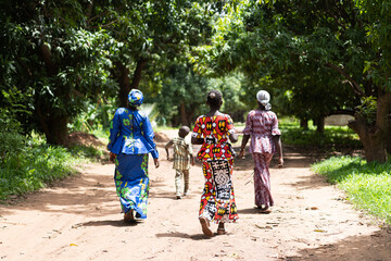 Group of black African villagers strolling along a dirt road among tropical trees - obrazy, fototapety, plakaty