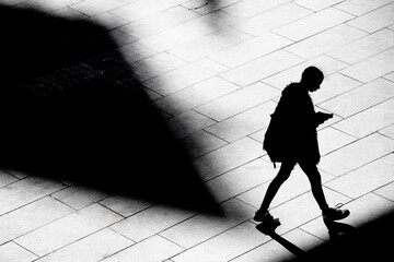 Shadow silhouette of teenage girl watching cell phone while walking city street sidewalk