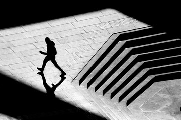 Shadow silhouette of teenage boy walking city street sidewalk, in black and white