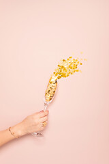 Woman's hand holding champagne or sparkling wine glasse with golden confetti over pink background. Christmas, new year party, birthday or wedding celebration idea. Top view, flat lay, copy space © netrun78