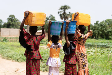 Four black African girls on their way to the village with full water continers on their heads