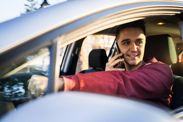 Young caucasian man using mobile phone talking and calling while driving or waiting in car real people mobile phone talk call in vehicle
