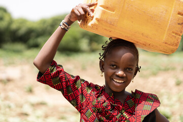 Portrait of a smiling black Africn girl carrying a water canister on her head