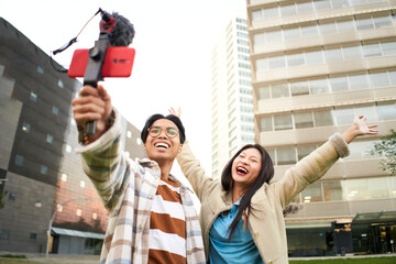 Happy asian couple taking a selfie in a city - Trendy young friends having fun with the technology trend - Concept of technology, friendship and influencer.