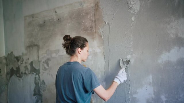 A professional repairwoman puts a plaster on the wall with a spatula. Female repairing the wall with a putty knife. The internal construction and finishing work. Young woman doing home repairs.