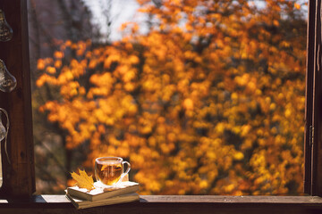 A cup of hot tea and open book on a vintage windowsill. Still life details in home on a wooden window. Read and rest. Cozy autumn concept.