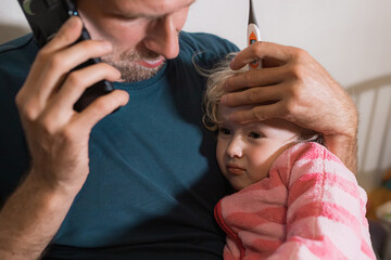 A caring lonely father consoles a sick girl after taking a high temperature with a thermometer and calls doctor