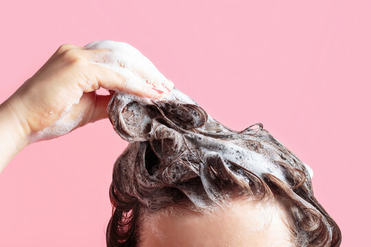 A girl washes her hair with shampoo on pink background, front view.